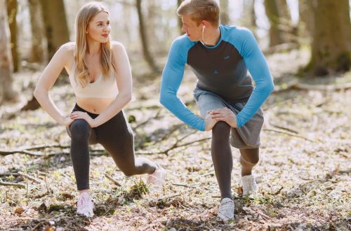 A couple engages in outdoor stretching exercises in a sunlit forest setting, promoting wellness and fitness.