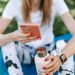 Woman using smartphone while holding bottle on yoga mat outdoors.